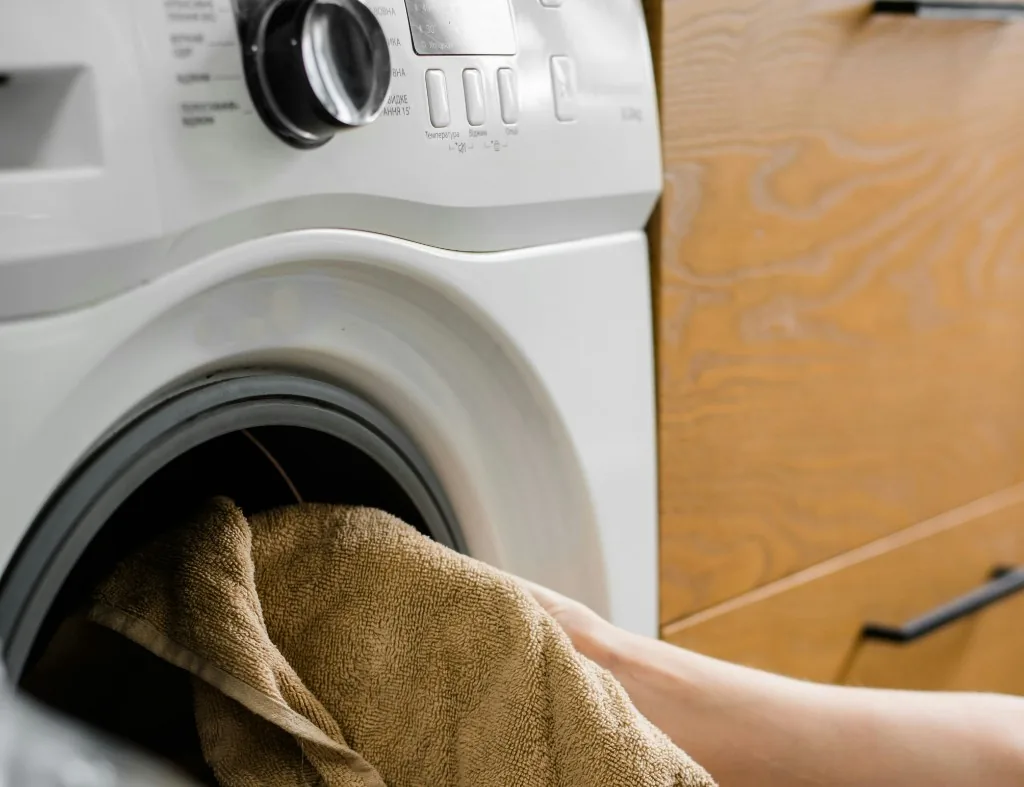 Hands placing a towel into a white front-load washer